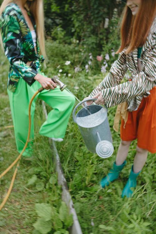 Free Two women in stylish outfits watering plants outdoors, highlighting gardening activities. Stock Photo