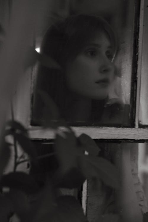 Grayscale Photo of Woman Looking Out the Window