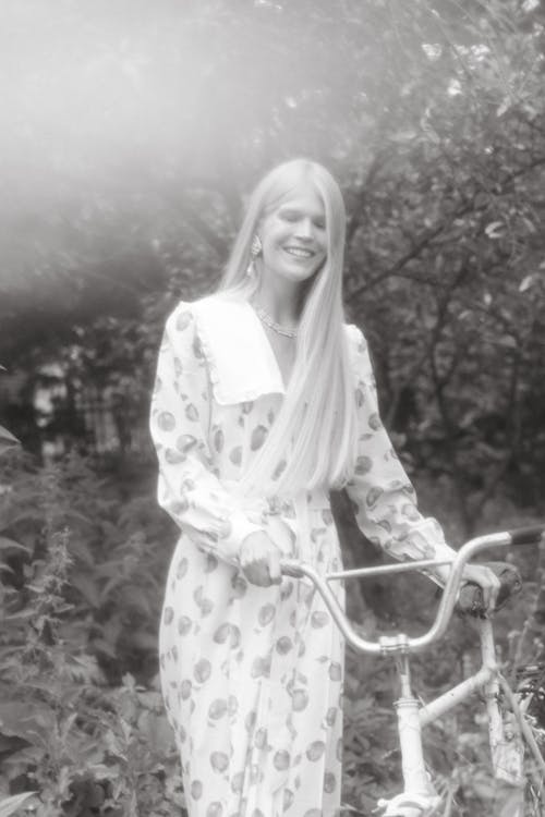 Grayscale Photo of Woman in Dress Holding a Bike 