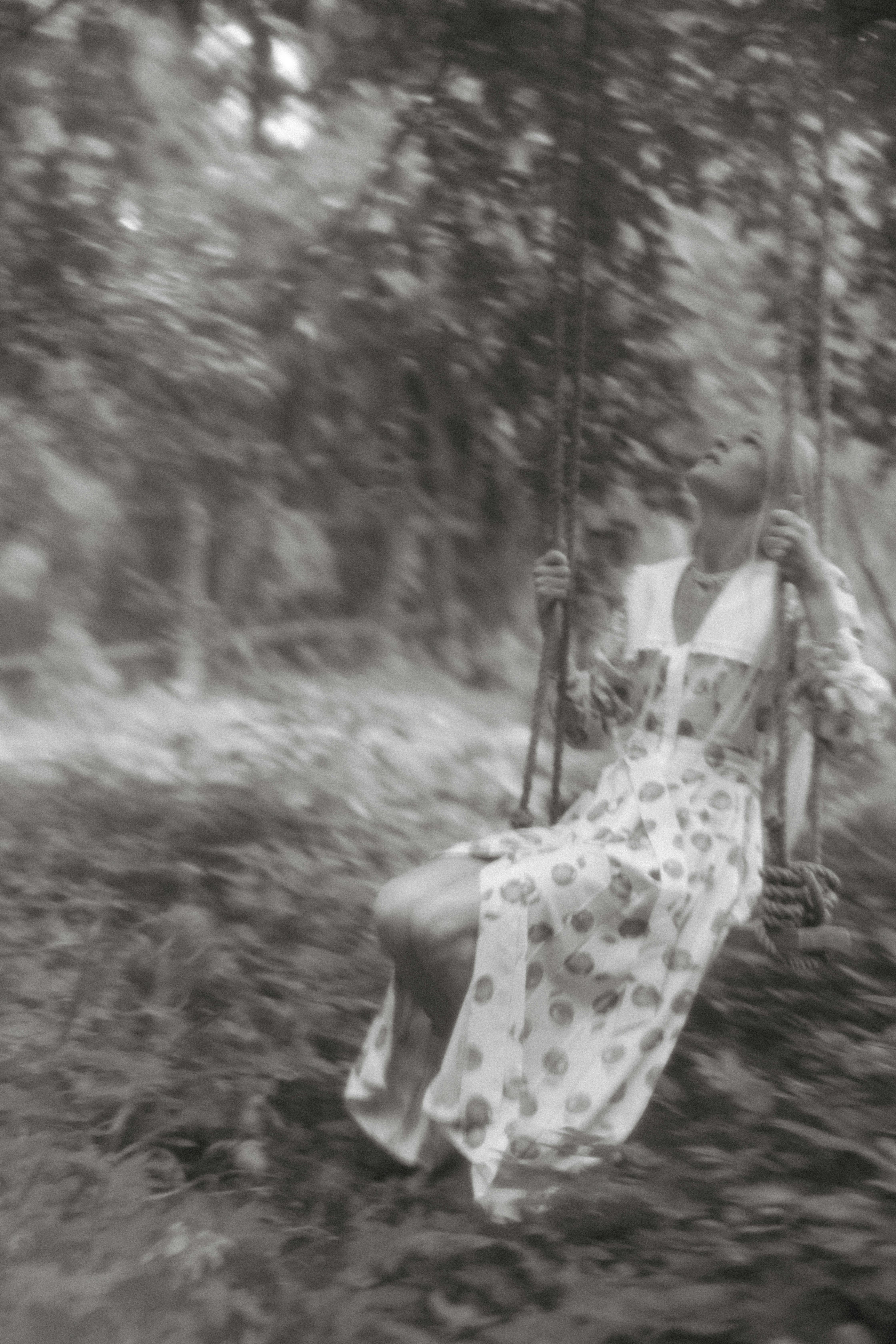 Elegant black and white portrait of a woman on a swing in nature, conveying a sense of nostalgia.
