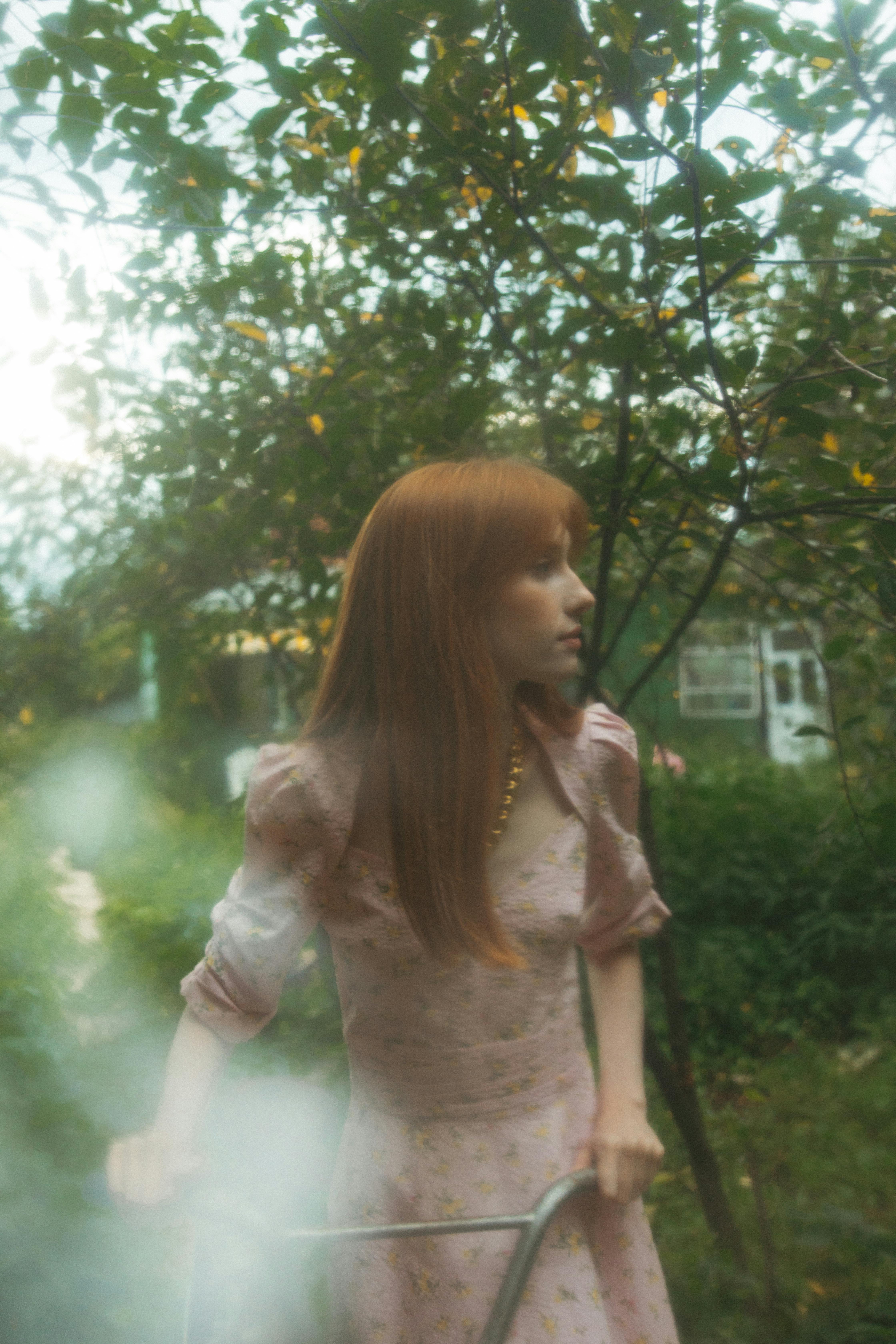 A woman in a floral pink dress walks in a lush garden, evoking a serene, dreamy atmosphere.