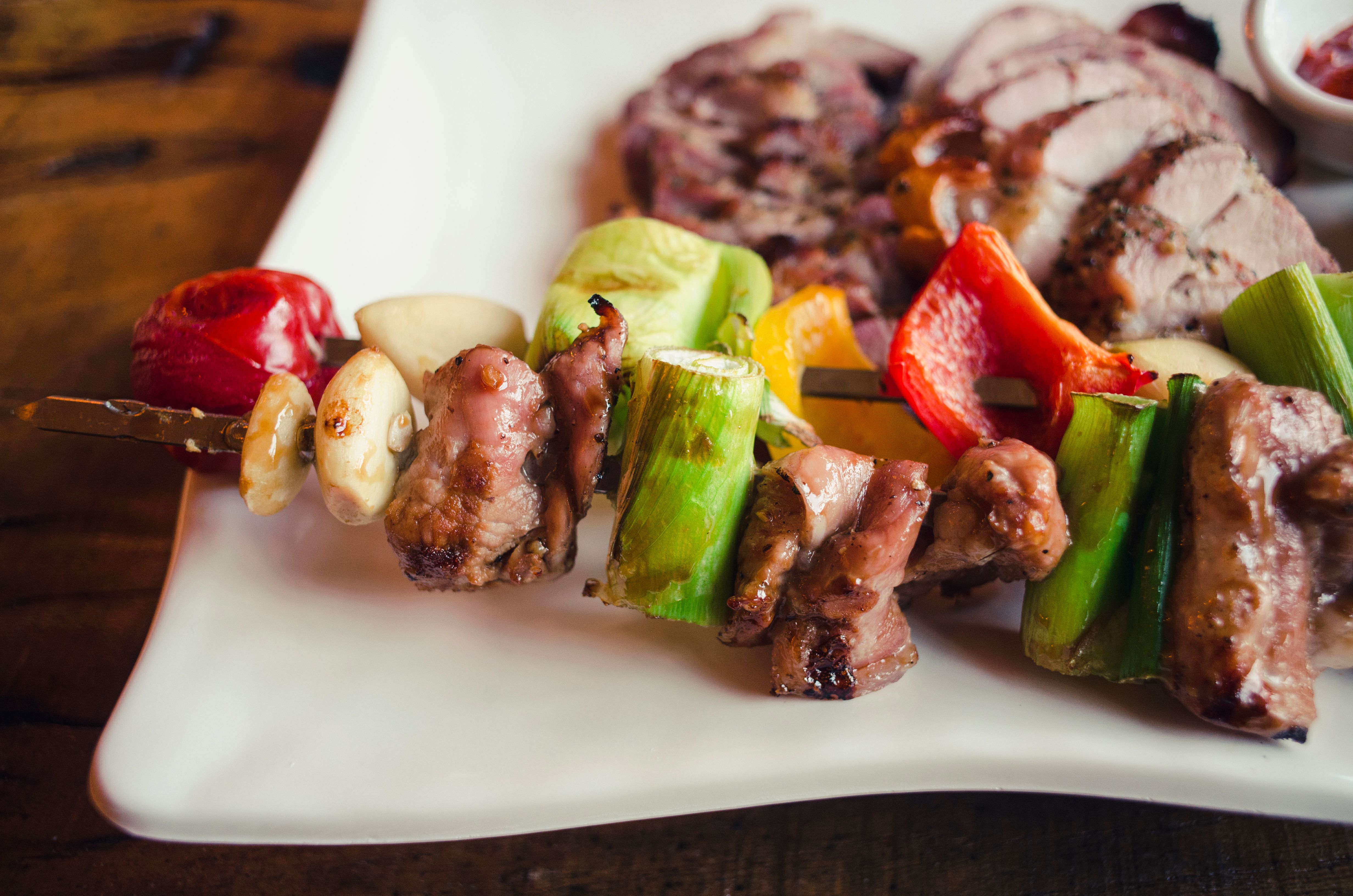 Golden-brown grilled pork and pineapple skewers on a white plate, glistening with scotch bonnet pepper glaze and garnished with lime wedges
