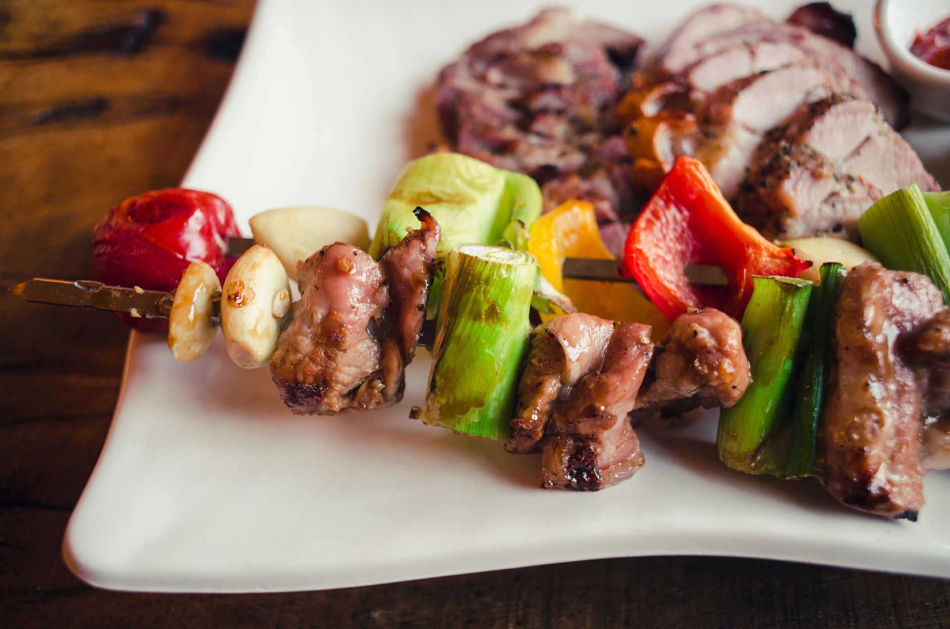 Golden-brown grilled pork and pineapple skewers on a white plate, glistening with scotch bonnet pepper glaze and garnished with lime wedges