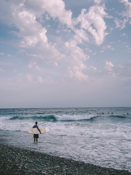 A Person Holding Surfboard while Standing at the Beach