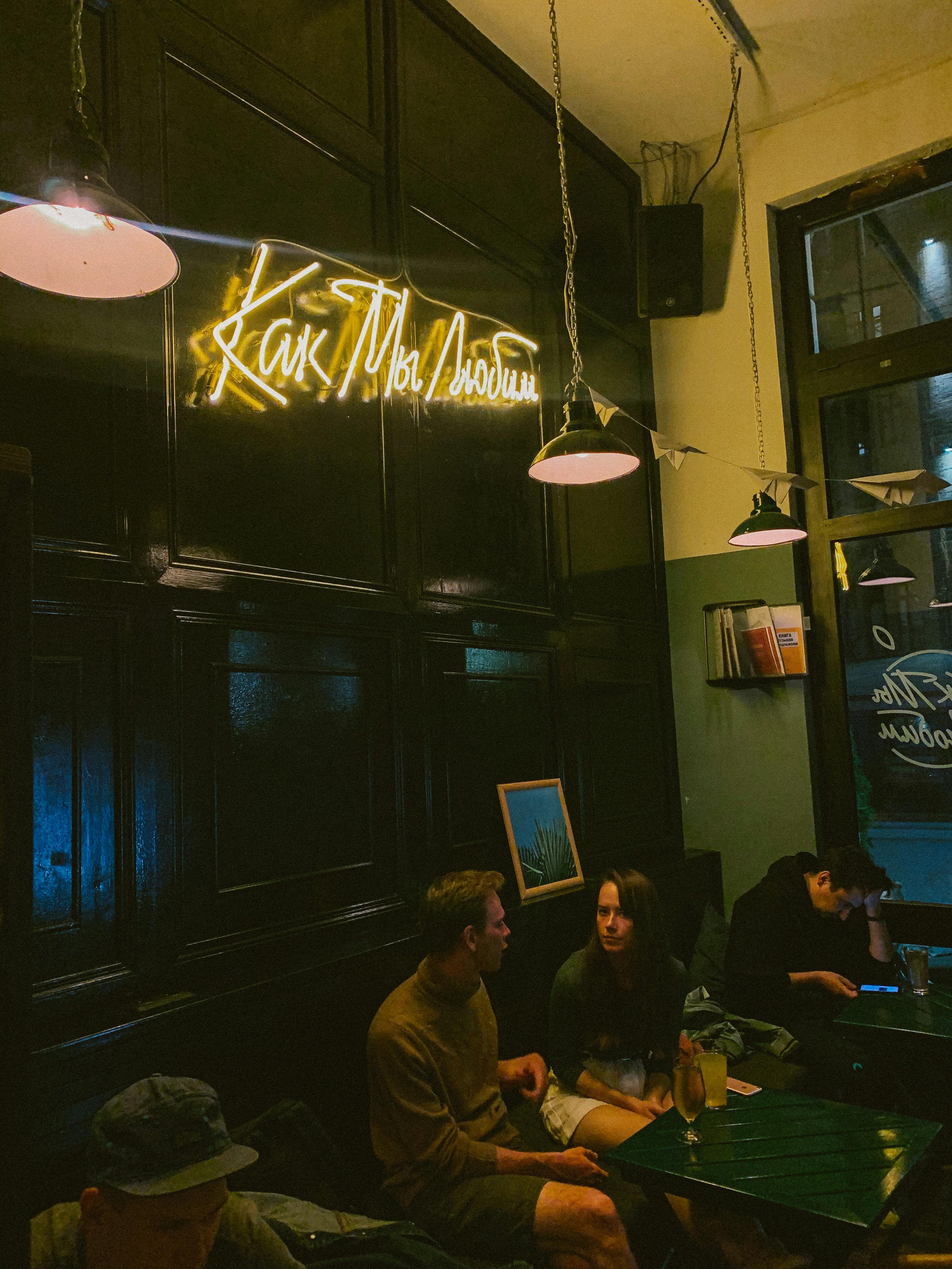 Two adults sharing a drink in a warmly lit cafe with neon sign decor.