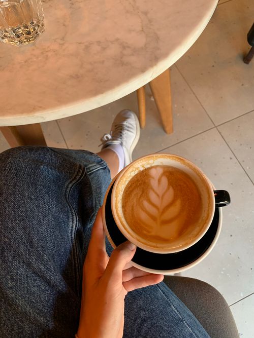 Free Person holding a latte with beautiful art in a cozy indoor cafe setting, showcasing a relaxed atmosphere. Stock Photo