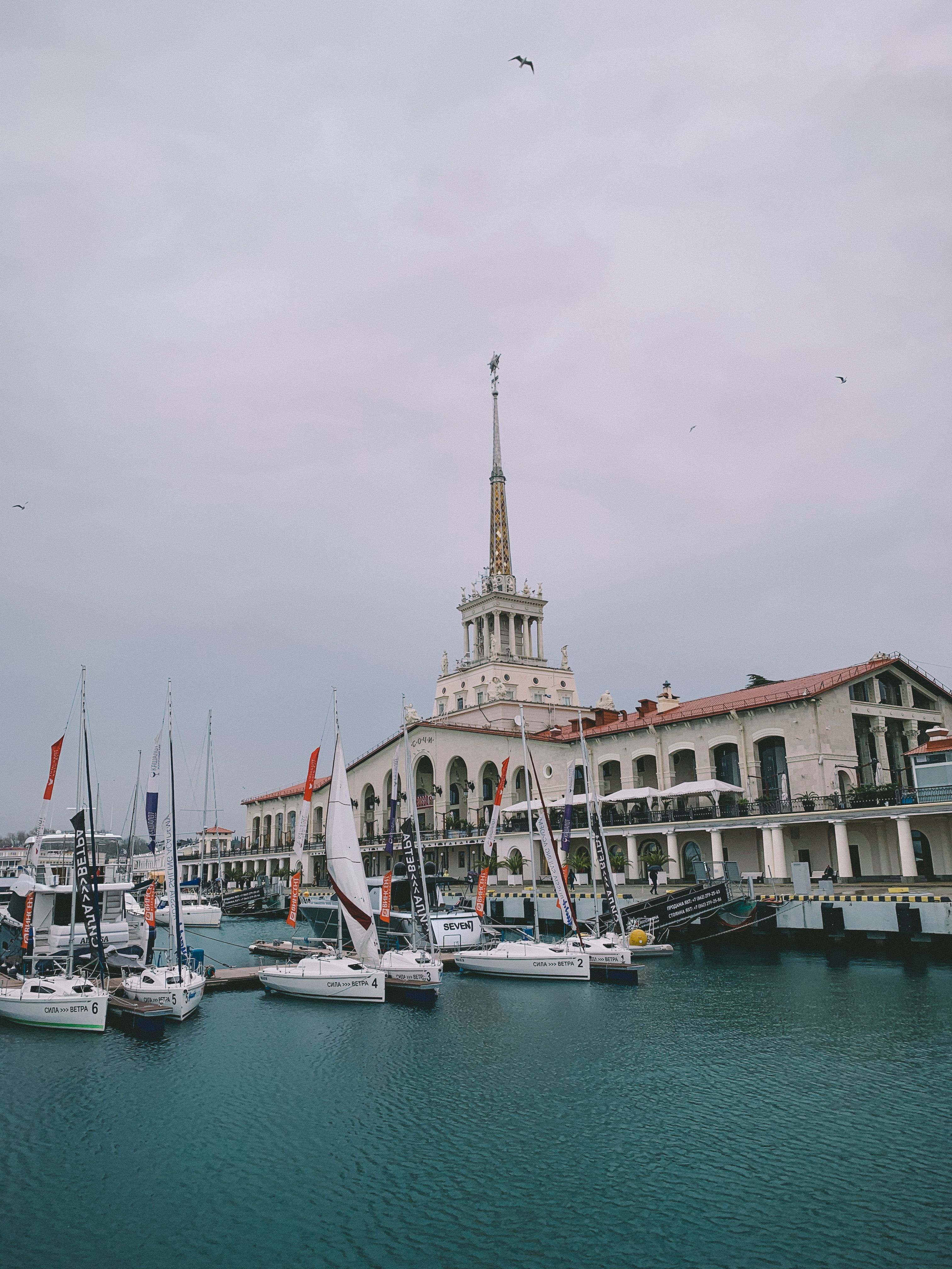 A picturesque marina scene with sailboats docked near a historic building on a cloudy day.