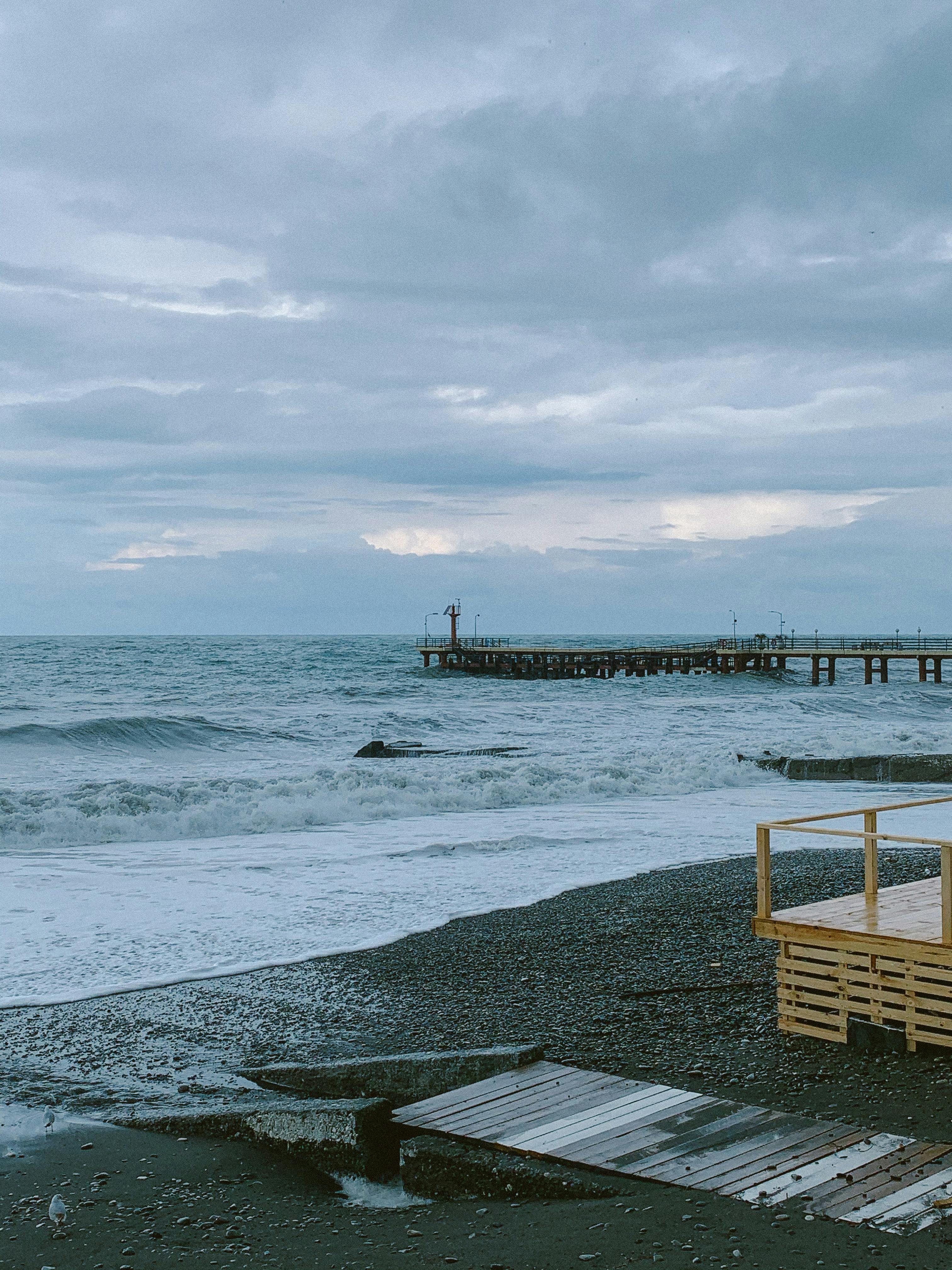 Serene overcast beach scene featuring waves, a wooden pier, and a cloudy sky.