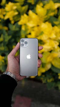 Hand holding a modern smartphone with yellow flowers in the background, showcasing technology blends with nature.