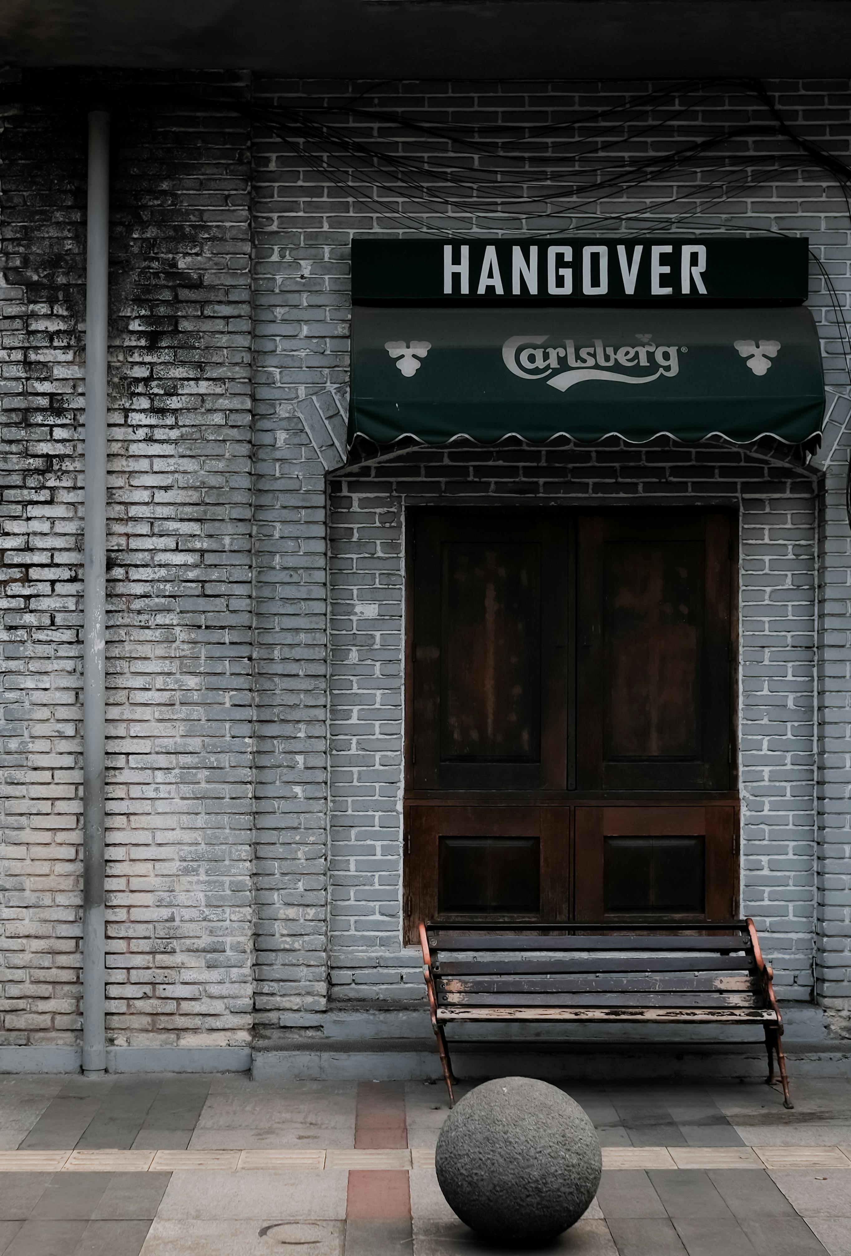 A rustic vintage bar entrance with a green awning, wooden bench, and brick wall facade.