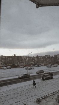 A snowy street scene with a person walking and cars parked, capturing winter's urban charm.