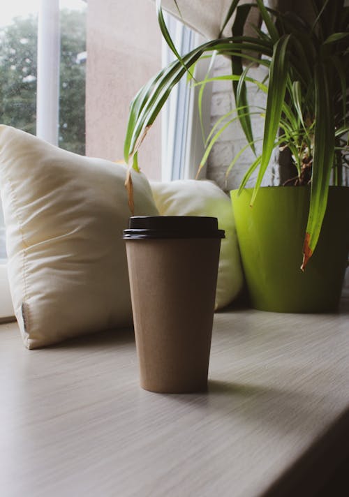 Brown Disposable Cups beside White Throw Pillow