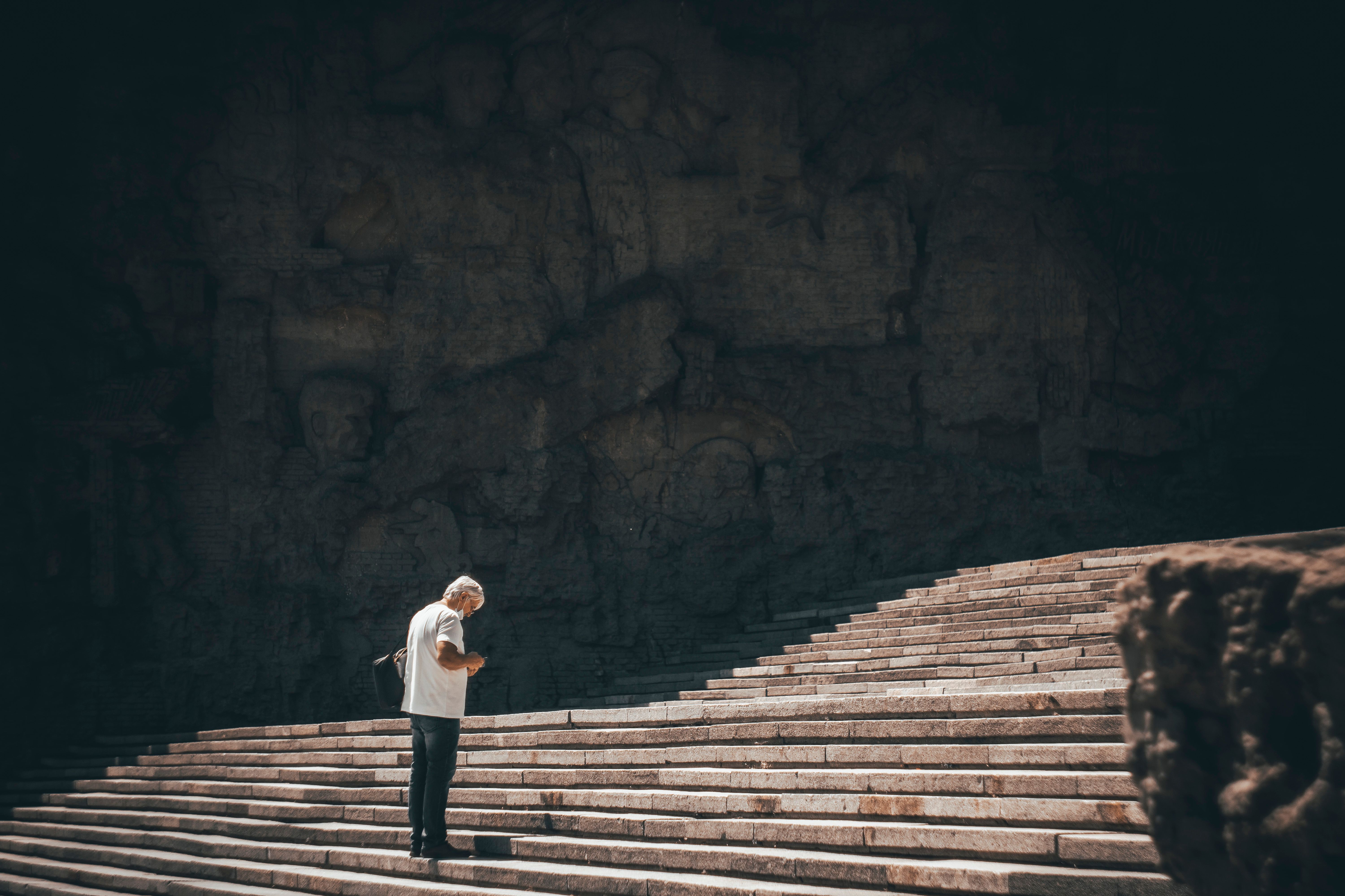 A lone man stands on expansive stone stairs under a dramatic shadow, capturing a moment of contemplation.