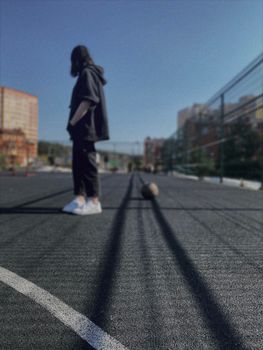 Silhouette of a person in a black outfit standing on a sunny basketball court.
