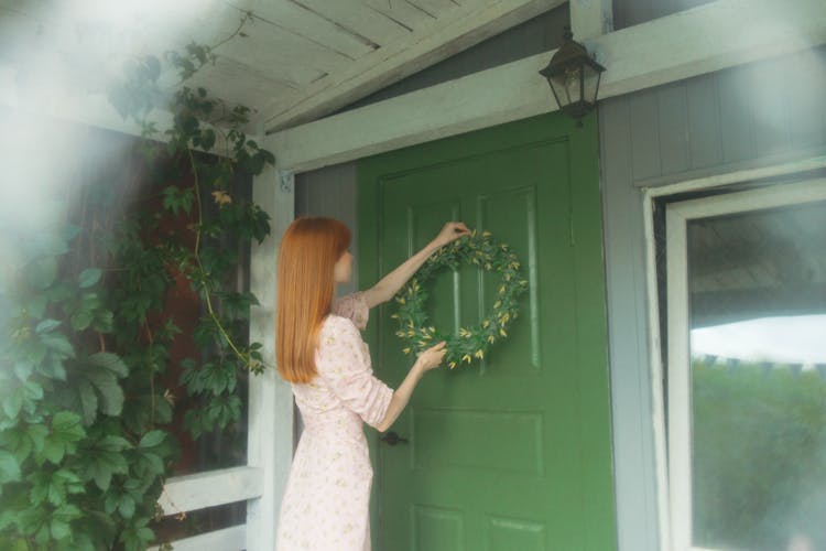 A Woman In White Dress Holding A Wreath By The Door