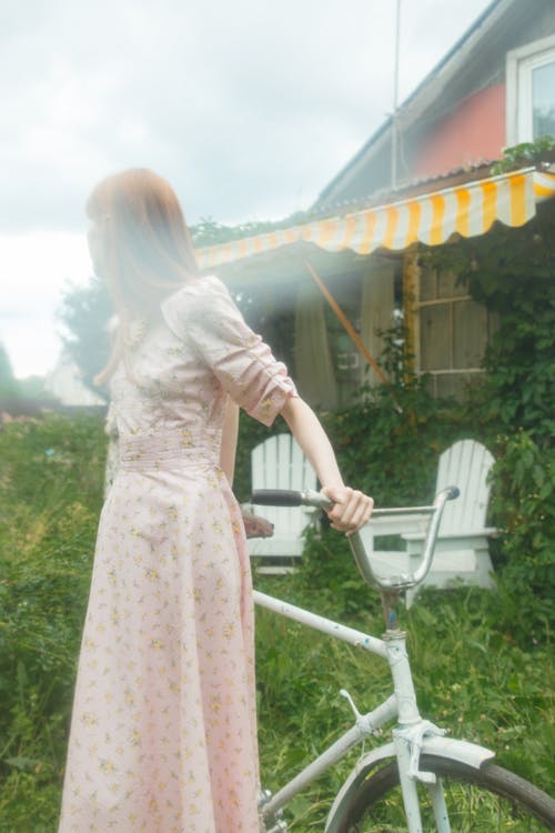 Woman in Pink Long Sleeve Floral Dress Holding on a Bicycle