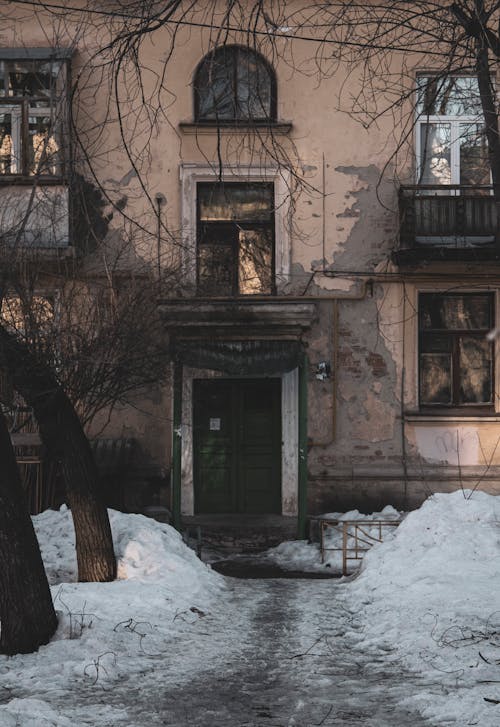 A Bare Trees on a Snow Covered Ground in Front of an Abandoned House