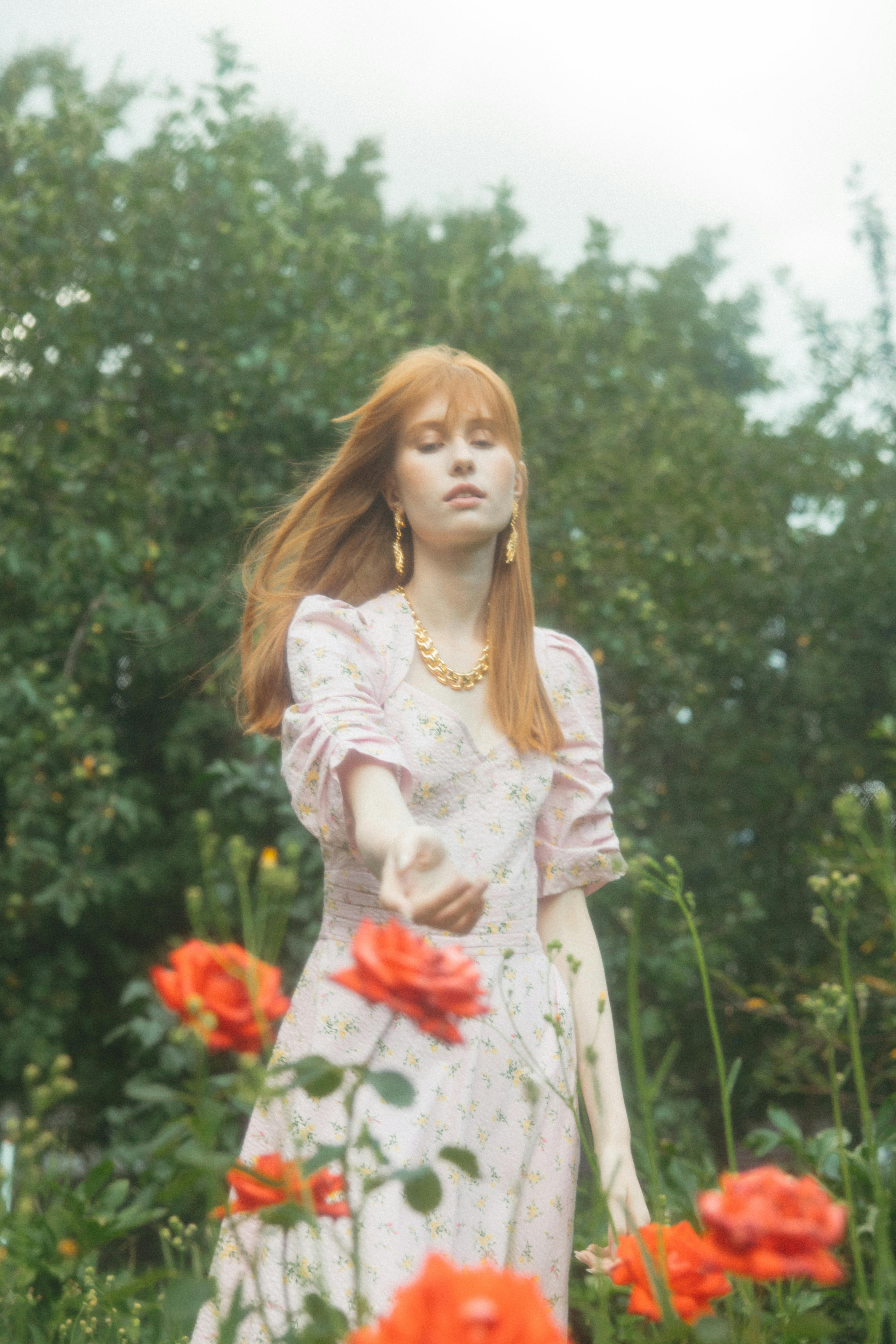 woman in pink floral dress standing beside red flower plant