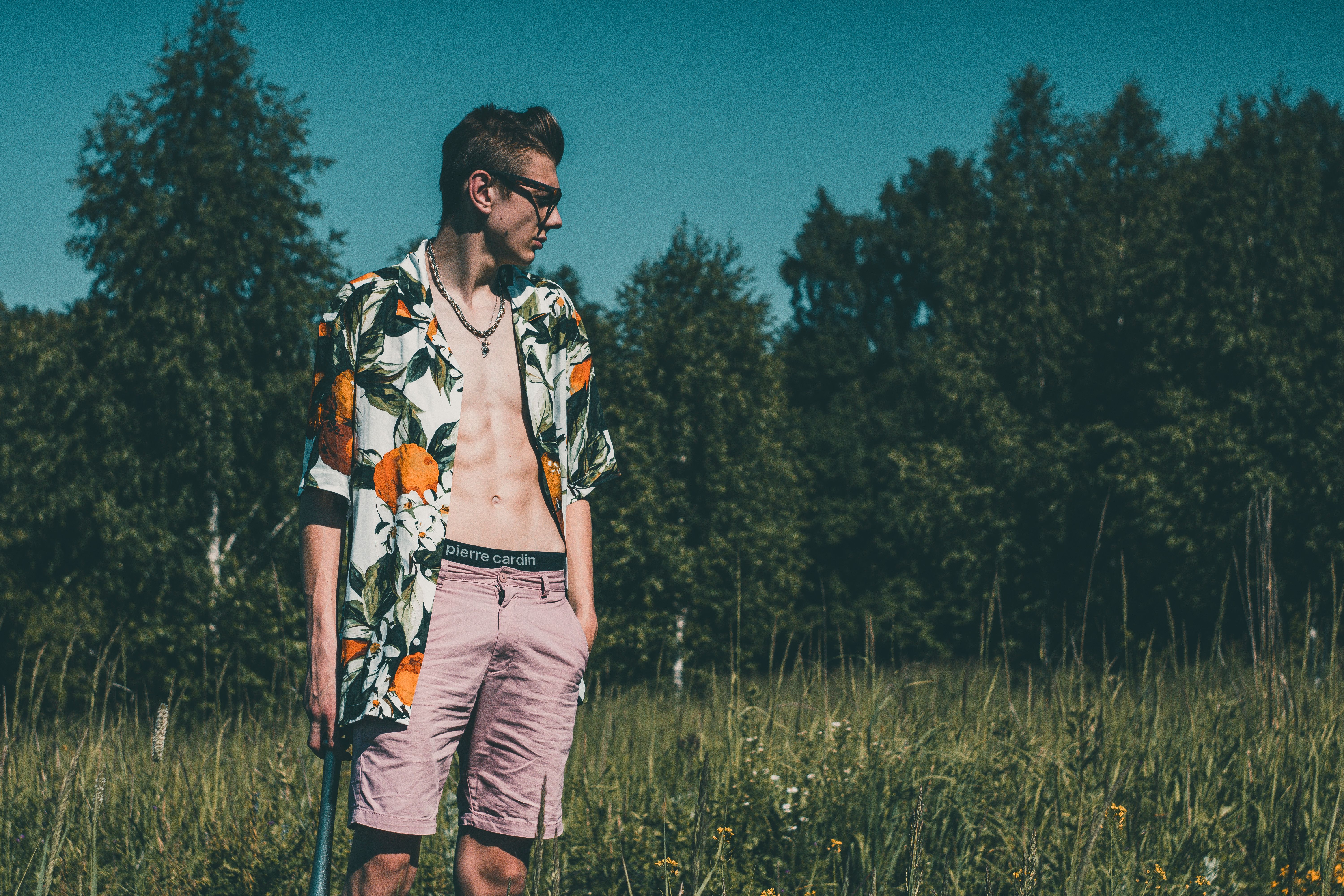 Fashionable young adult in floral shirt standing in a meadow on a sunny day.