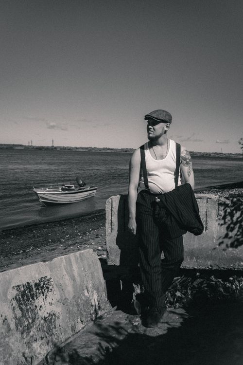 Free A stylish man in a beret stands by the shore in a monochrome scene, exuding vintage charm. Stock Photo