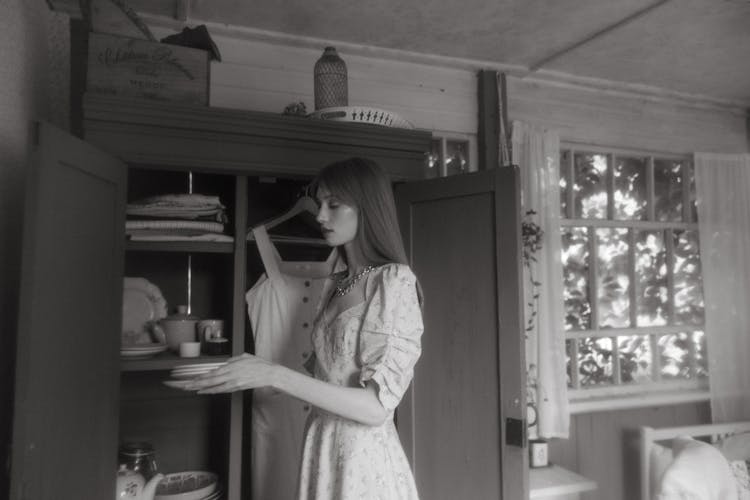 A Woman Holding Plates Near A Wooden Cabinet