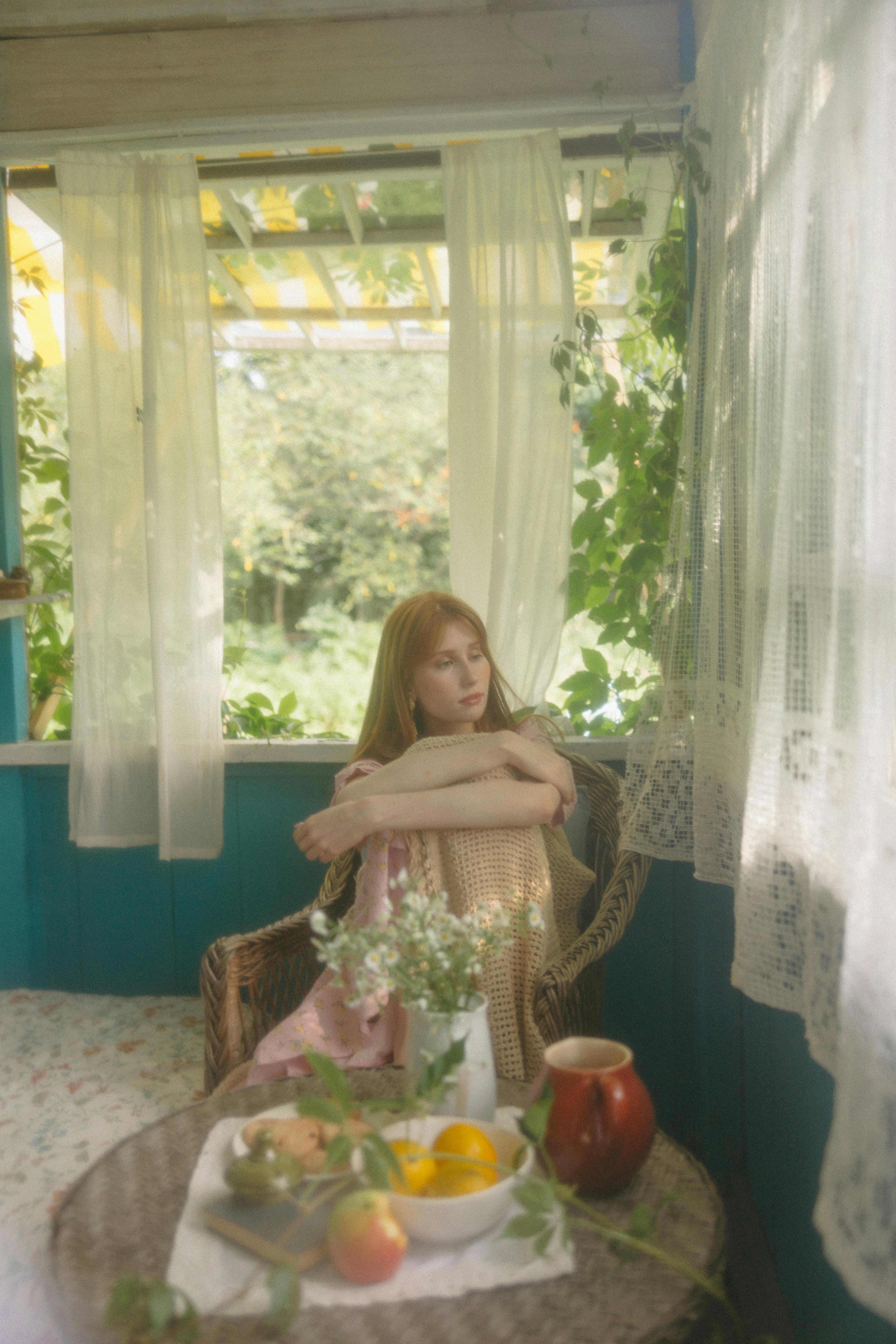 A contemplative woman by the window in a vintage room, embracing peacefulness.