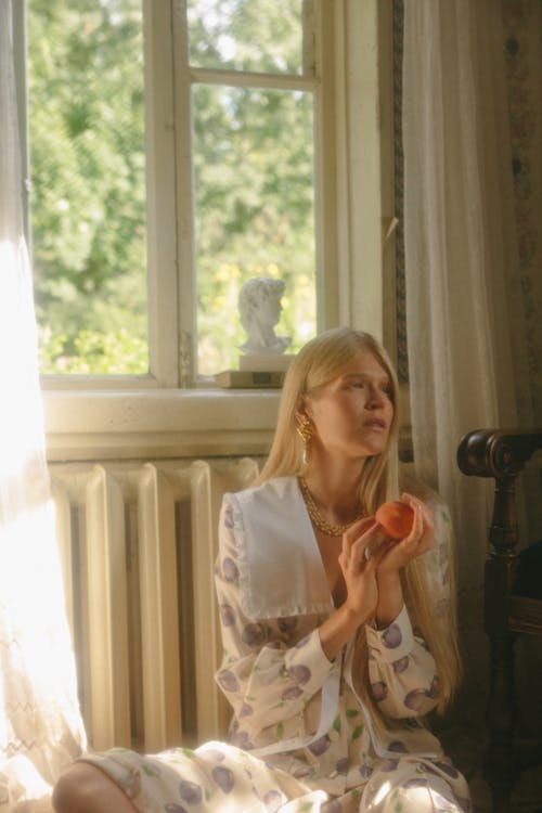 A Woman Holding a Piece of Fruit Sitting by the Window