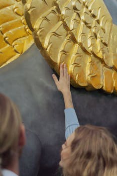 A person reaches out to touch a golden wing on a large statue, capturing a moment of interaction.