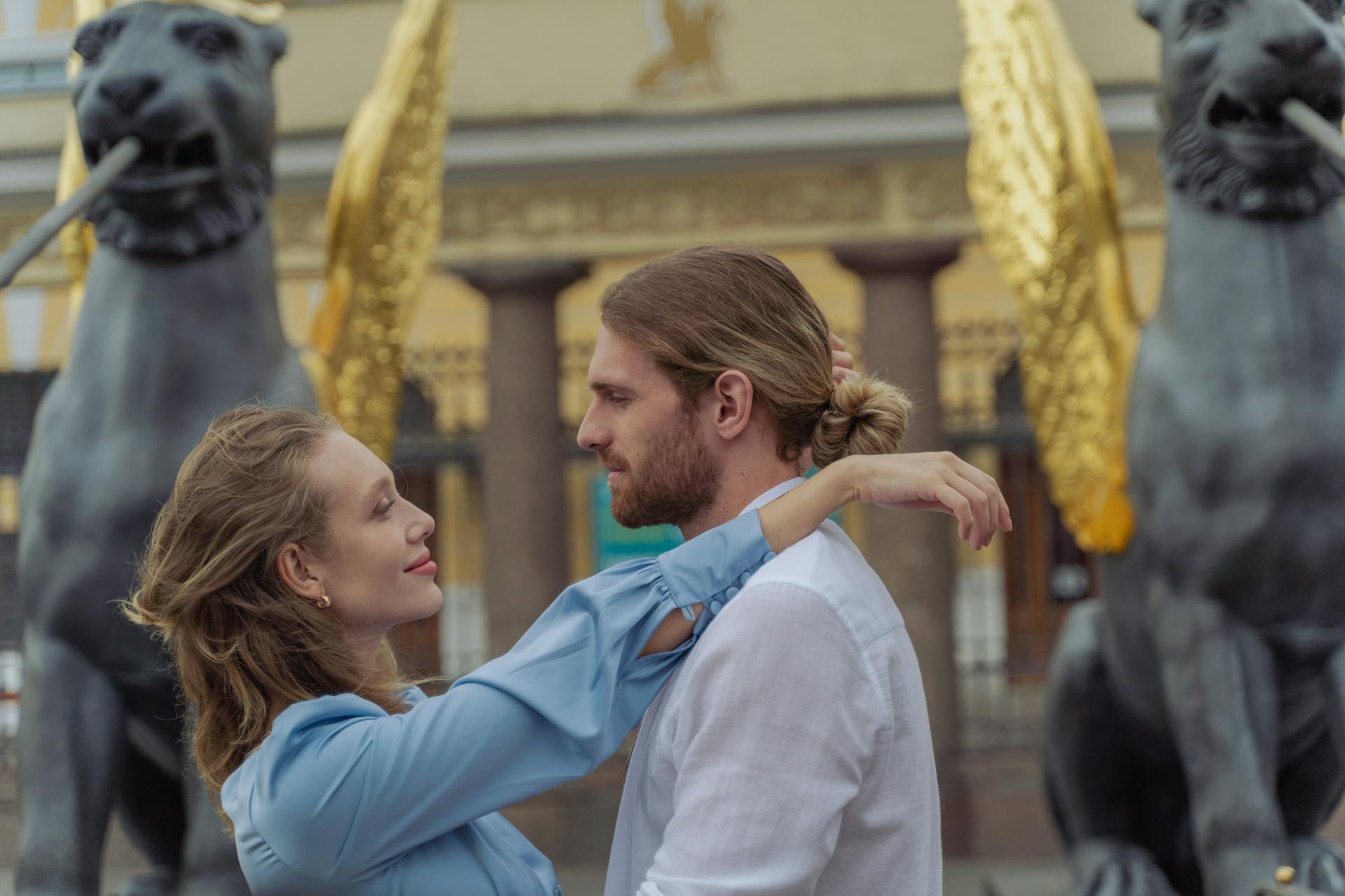 A loving couple embracing near ornate iron sculptures depicting golden creatures.