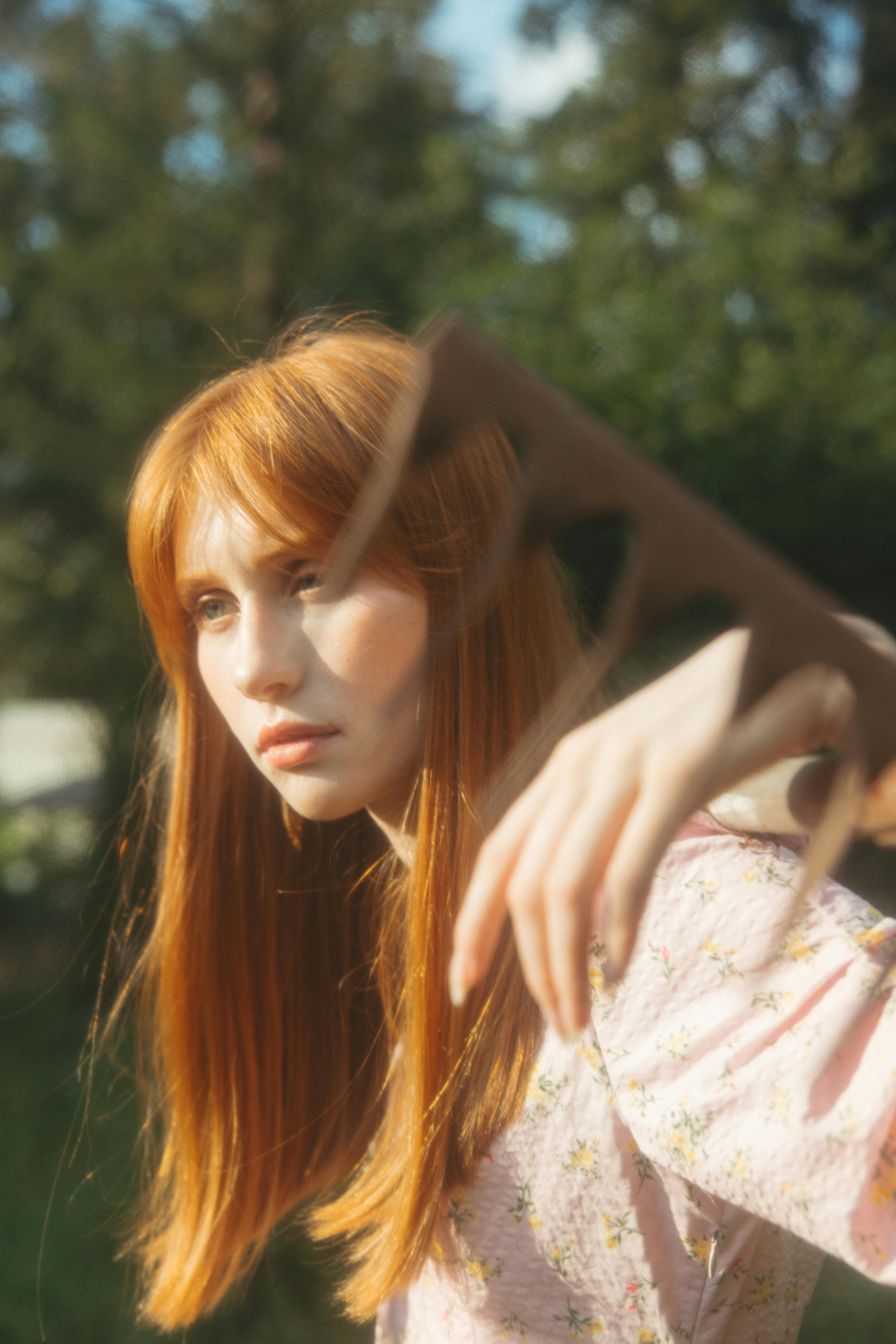 一位身穿花卉连衣裙的红发女子的艺术肖像，前景中有一只模糊的手