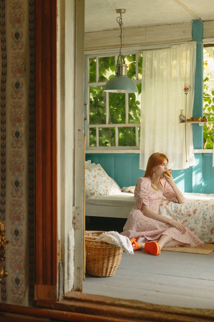 A Woman In A Pink Dress Eating A Fruit While Sitting On The Floor