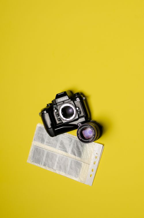 Free A top view of a black Nikon camera with lens and film negatives on a vivid yellow background. Stock Photo