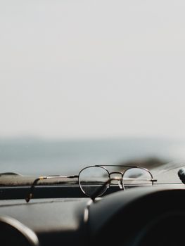 Minimalist still life of eyeglasses on a car dashboard with blurred outdoor view.