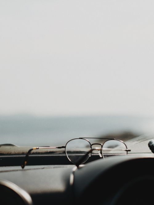 Free Minimalist still life of eyeglasses on a car dashboard with blurred outdoor view. Stock Photo
