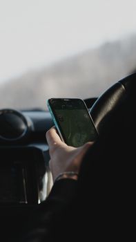 Close-up of a person using a smartphone for car navigation on a sunny day.