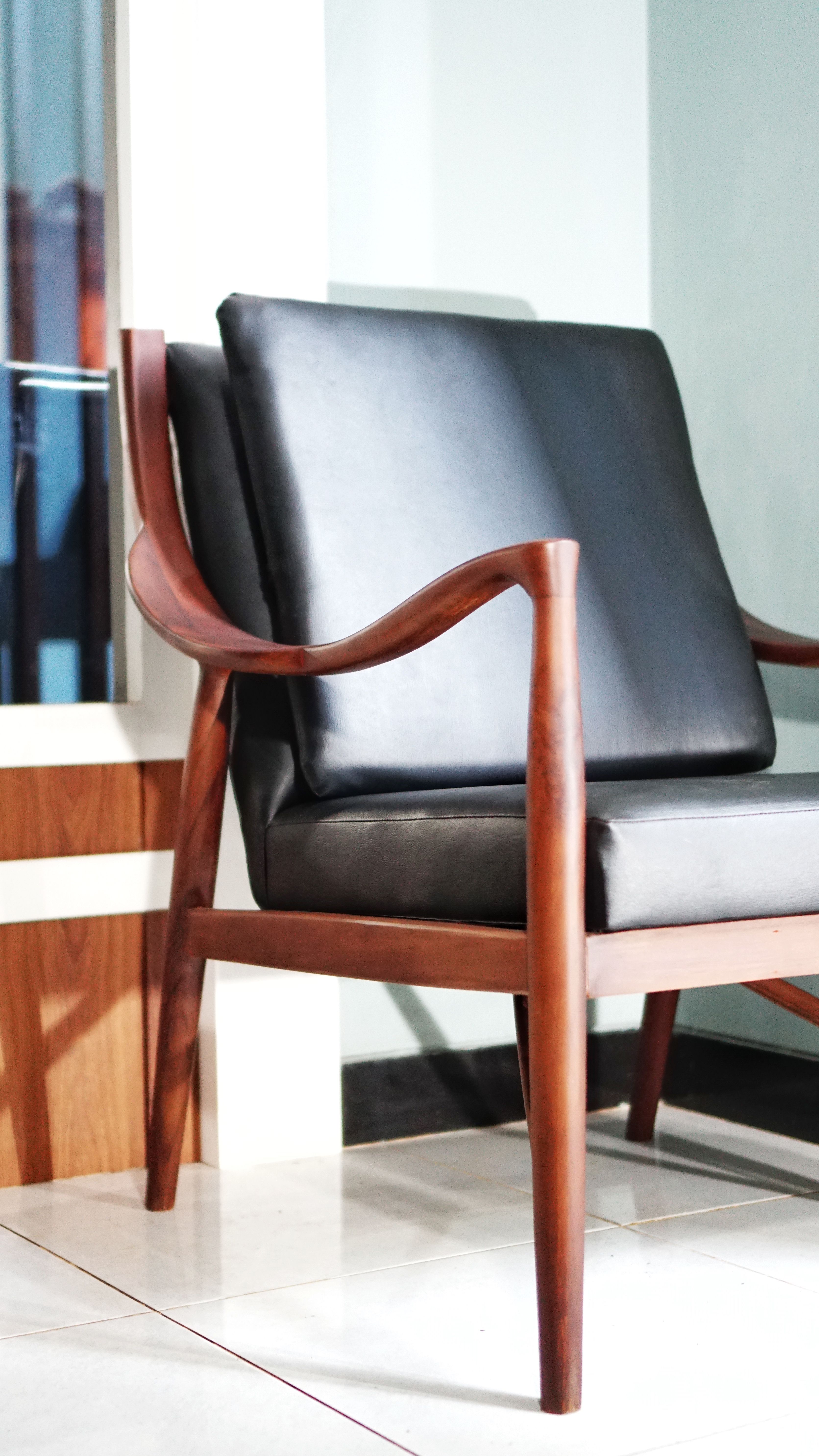 Stylish wooden chair with black leather seat in a modern indoor setting.
