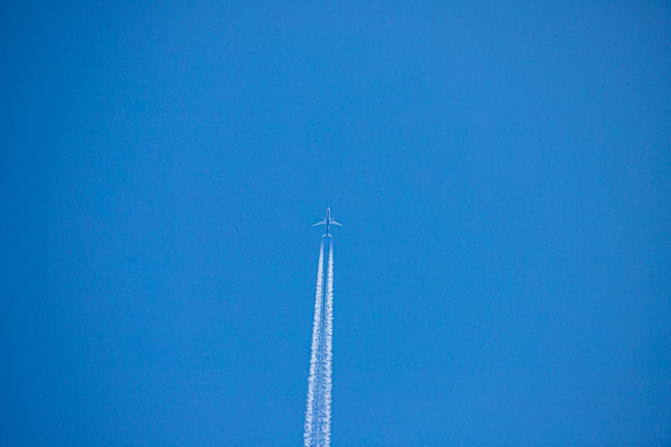 Fotomural Un avión volando alto dejando estelas contra un cielo azul claro, capturando la esencia del vuelo.