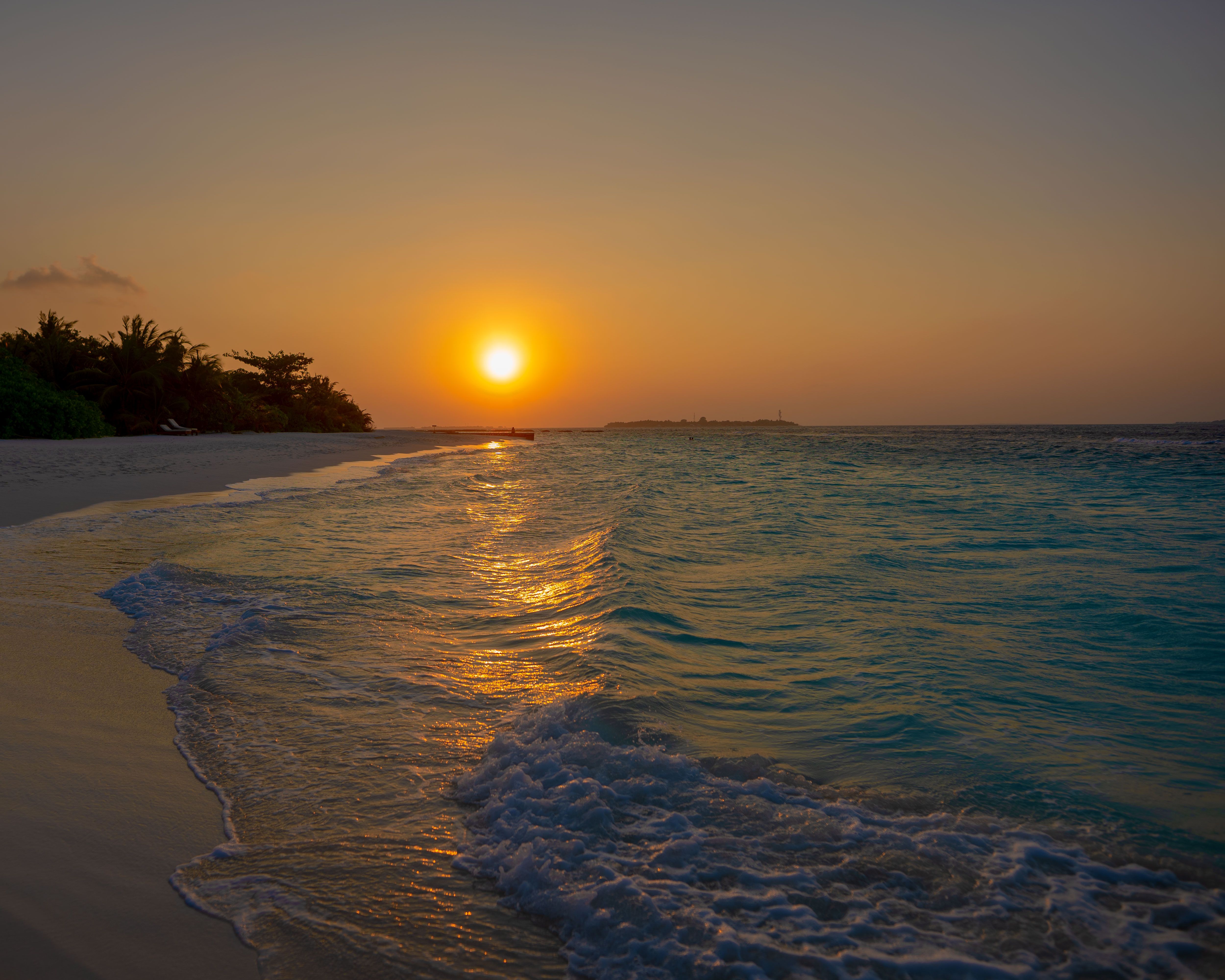 A breathtaking view of the sunset over a tropical beach with gentle waves crashing on the shore.