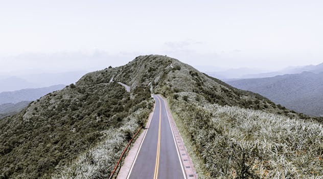 A winding road leading through lush green mountains under a clear sky.