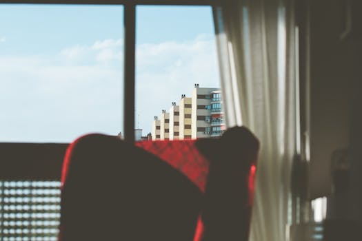Contemporary cityscape seen through glass window with red chair and curtains.