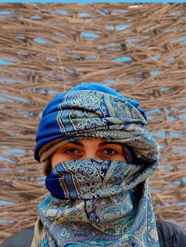 户外特写镜头中，一个人戴着一条五颜六色、有图案的蓝色围巾，背景是编织物