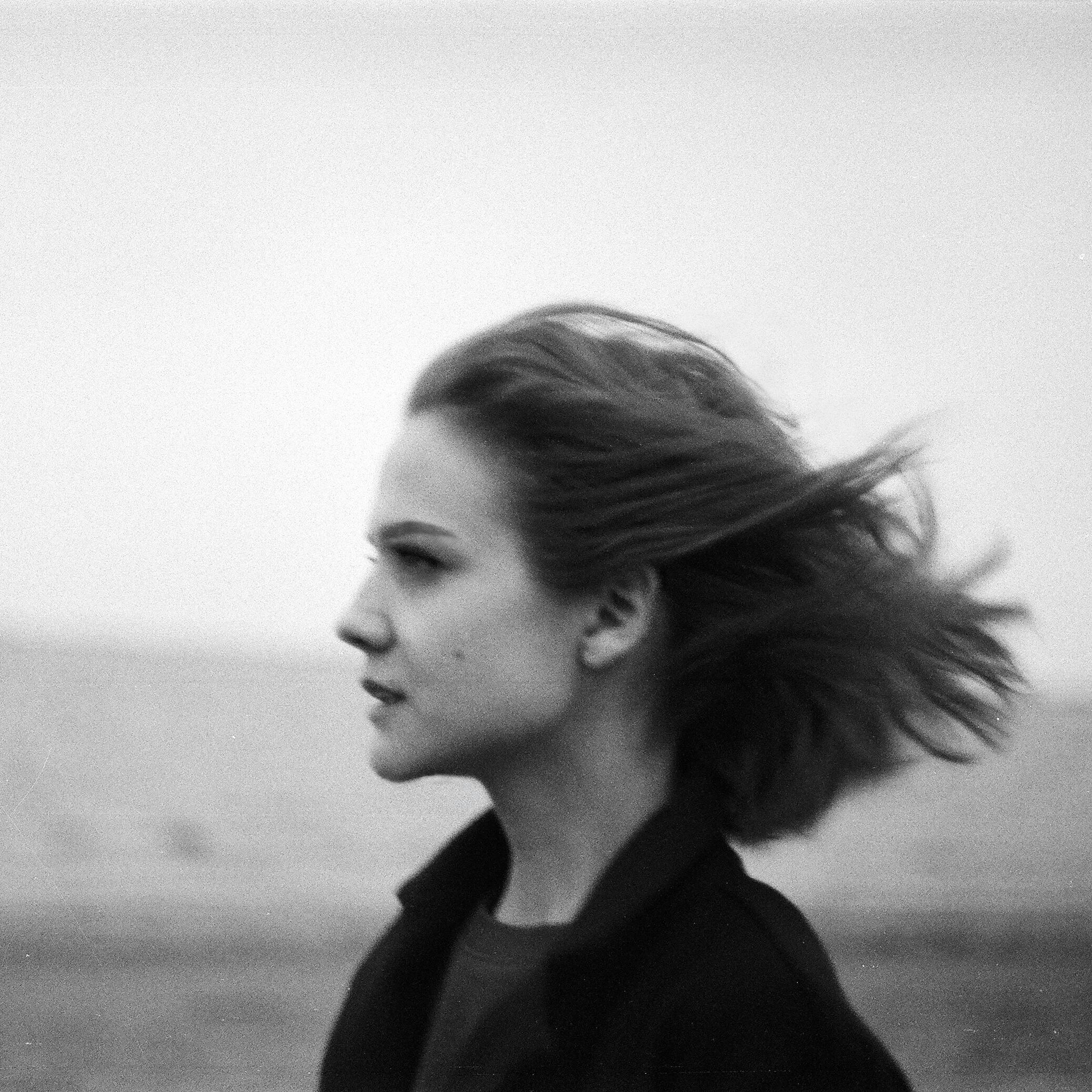 Monochrome side view of a woman with wind-blown hair by the ocean.