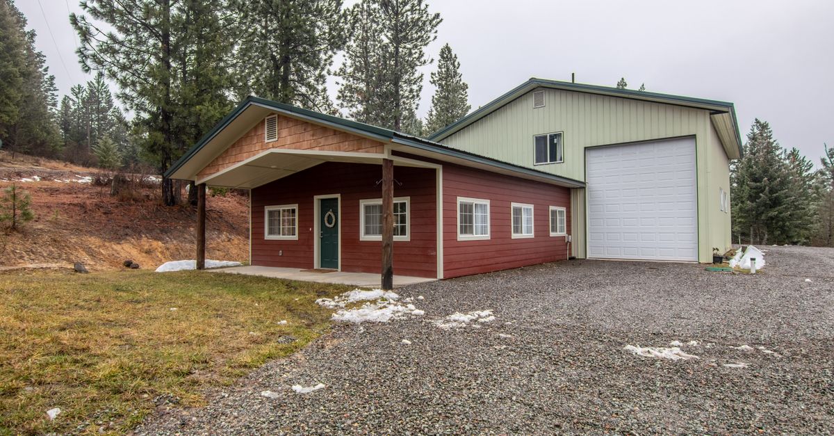 Charming detached rural house with garage surrounded by trees and light snow coverage.