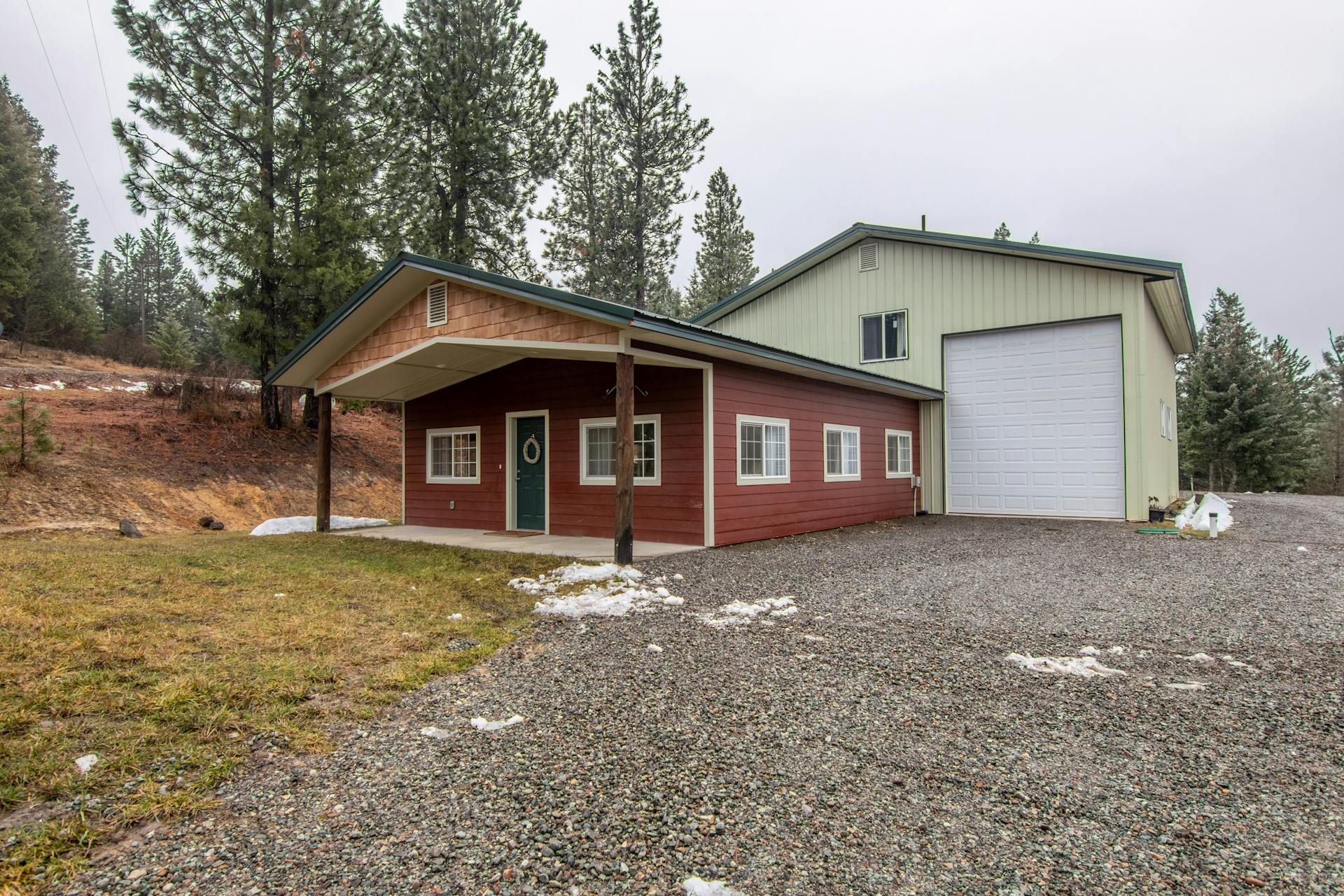 Charming detached rural house with garage surrounded by trees and light snow coverage.