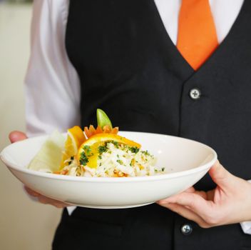 Waiter holding a white bowl with a fresh citrus salad, garnished with herbs. Perfect for dining themes.