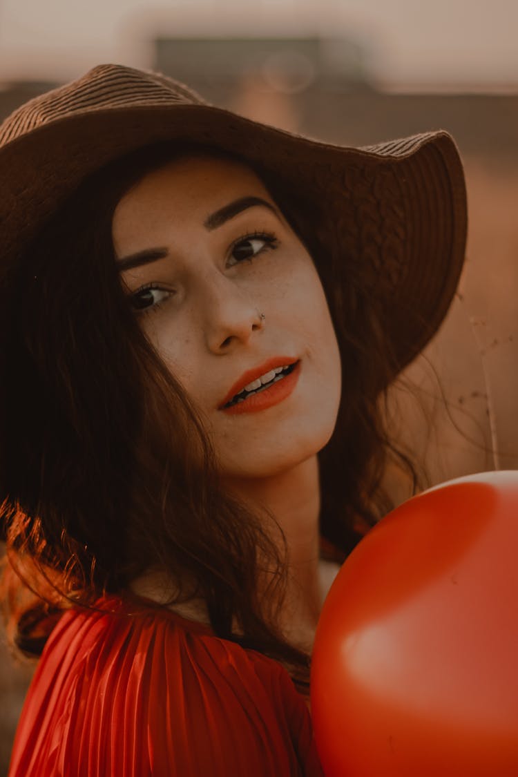 A Woman Wearing A Brown Hat Holding A Red Balloon