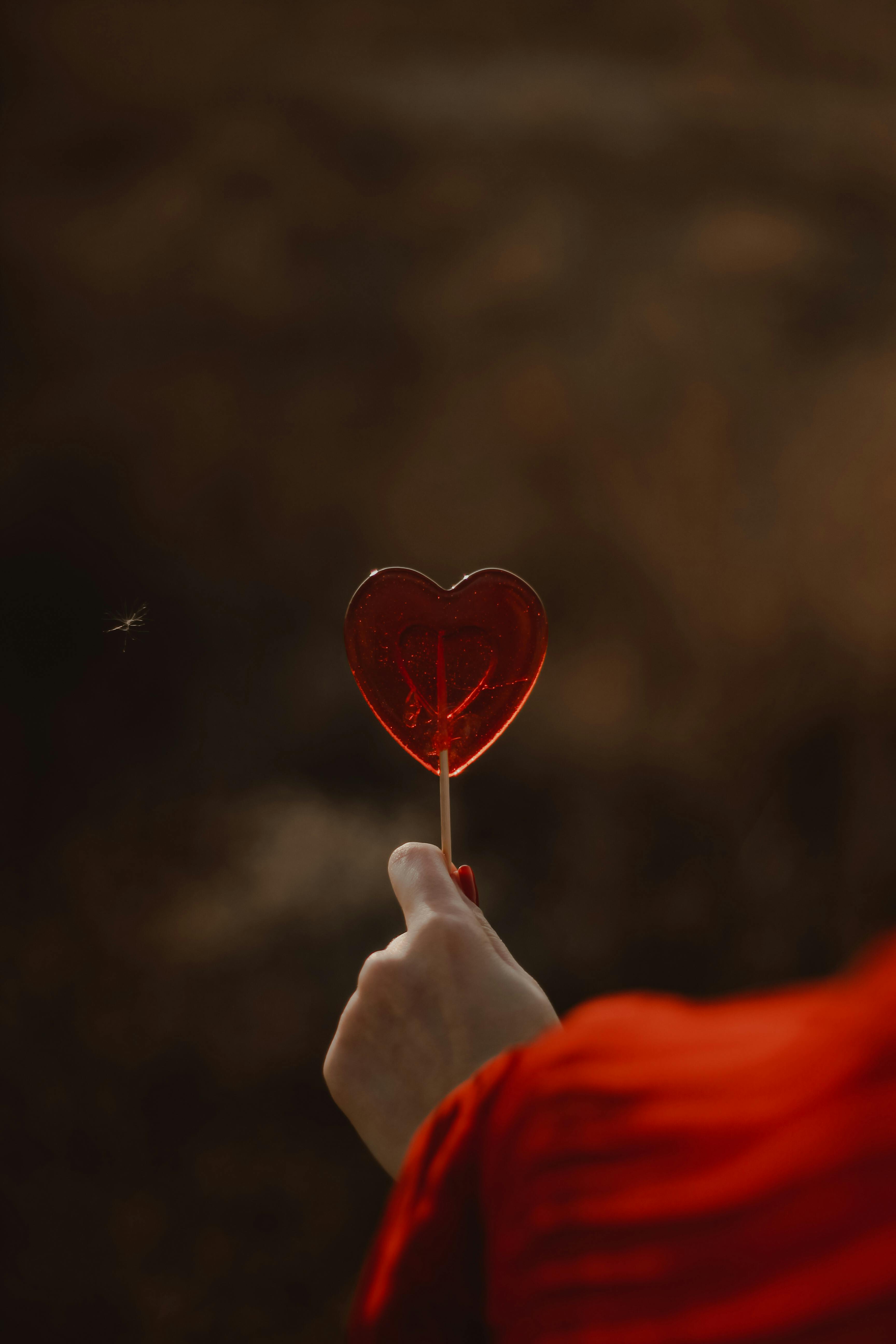 Close-up of a heart-shaped lollipop being held against a blurred outdoor background.