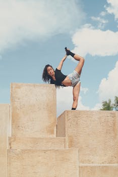 A woman balances in a yoga pose on large stone blocks against a clear sky.
