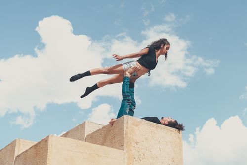 Free A man and woman performing an acrobatic balance act on a stone structure under a clear blue sky. Stock Photo