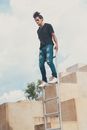 Man in Black T-shirt and Blue Denim Jeans Standing on Brown Concrete Stairs